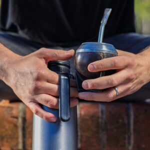 Inicio Close-up of hands holding a mate cup and thermos outdoors in Uruguay.
